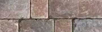 A close-up view of rectangular stone pavers in shades of grey, tan, and brown, arranged in a running bond pattern.