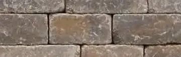 A close-up of a wall made of rectangular, weathered, gray and brown stone pavers stacked in a standard running bond.