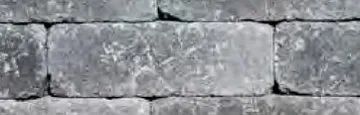 A close-up view of a wall made of rectangular, weathered gray stone bricks with a textured, mottled surface.