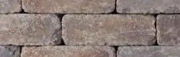 A close-up view of a wall made of rectangular, weathered stones in shades of brown, gray, and earthy tones.