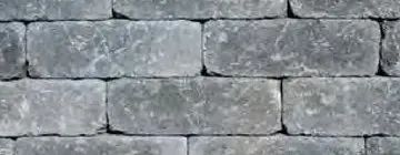 A close-up view of a wall made of rectangular, weathered gray stone blocks with visible texture and mortar joints.