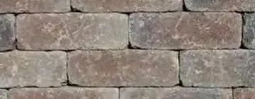 A close-up of a wall made of rectangular, rustic pavers in varying shades of brown, grey, and weathered stone.