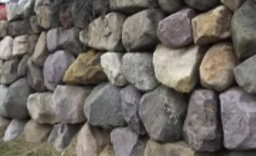 A close-up of a stacked stone retaining wall featuring large, rough-hewn rocks in various shades of gray, tan, and brown.