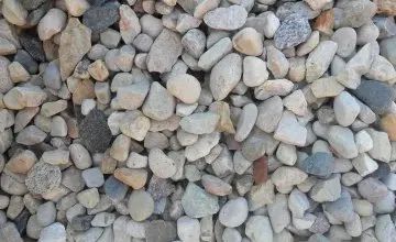 A close-up view of a pile of mixed-color gravel, featuring various shades of gray, beige, and white stones.