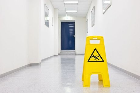 Yellow wet floor sign in a bright hallway with white walls and a blue door