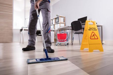 Person mopping office floor beside a yellow wet floor sign and cleaning cart.