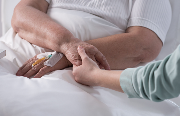 A woman is holding the hand of an elderly woman in a hospital bed.