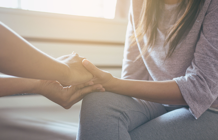 A woman is holding another woman 's hand while sitting on the floor.