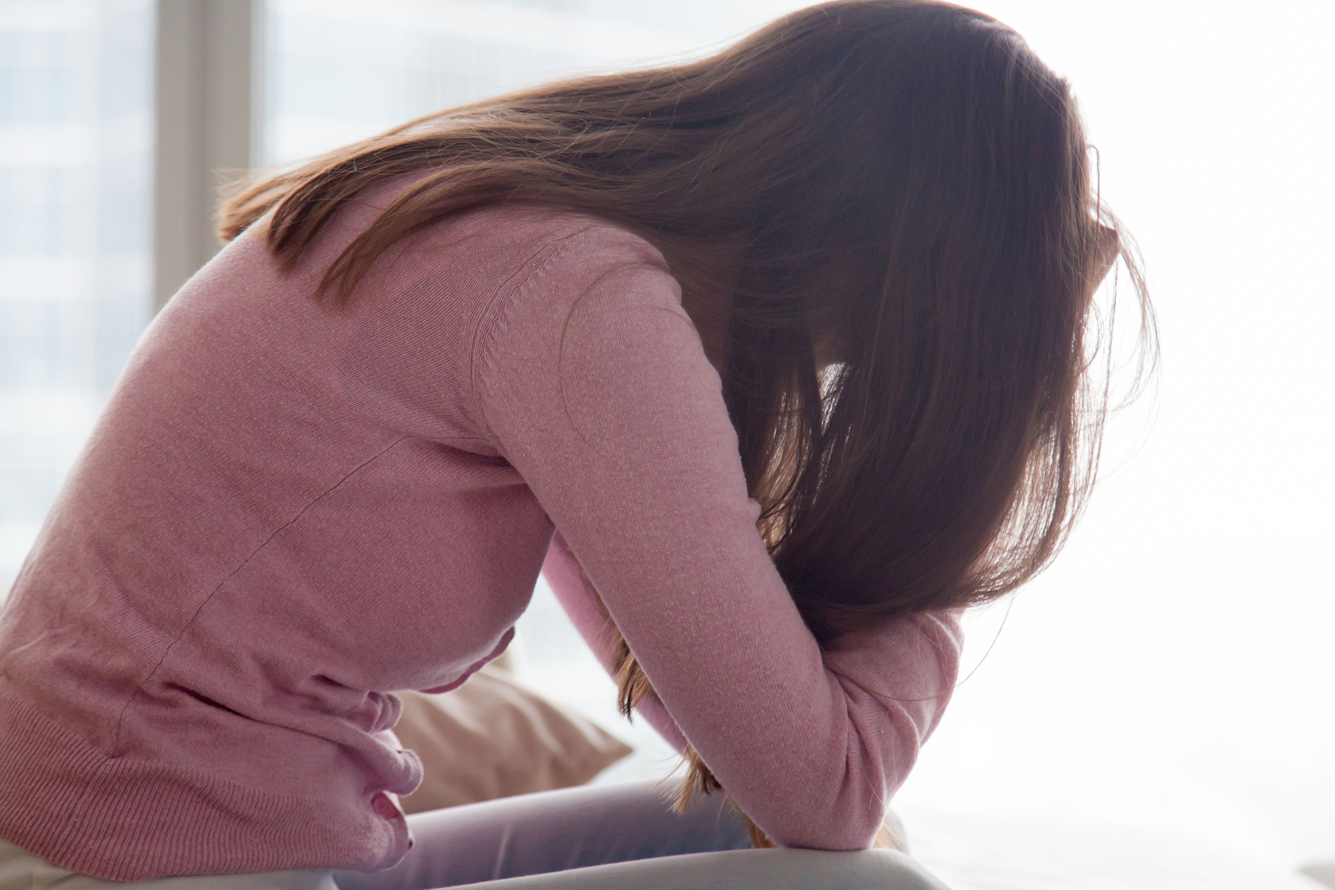 a woman in a pink sweater is sitting on a bed with her head down