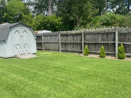 A barn is sitting in the middle of a lush green lawn next to a wooden fence