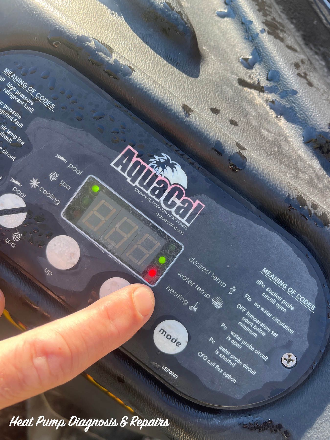 A finger points to the digital control panel of an AquaCal pool heat pump showing an error light.