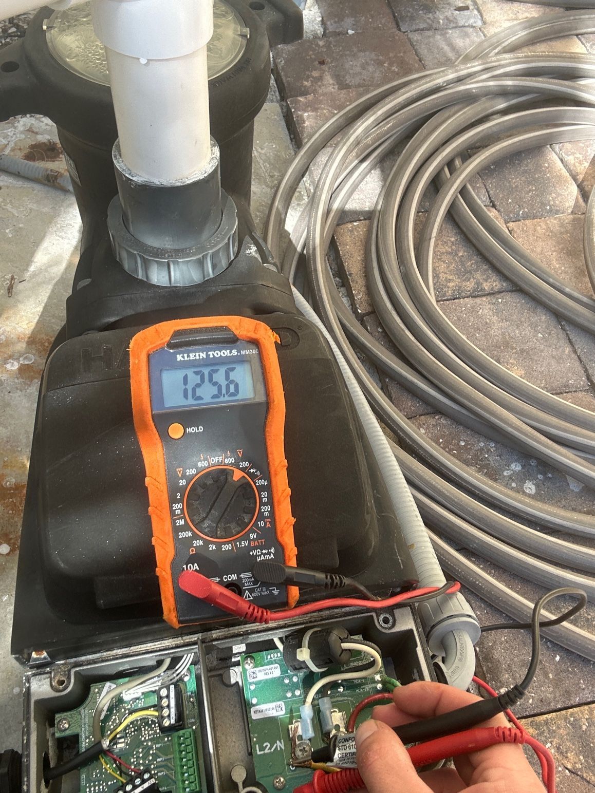 A multimeter showing a reading of 125.6 while testing the electrical components of a pool pump housing.
