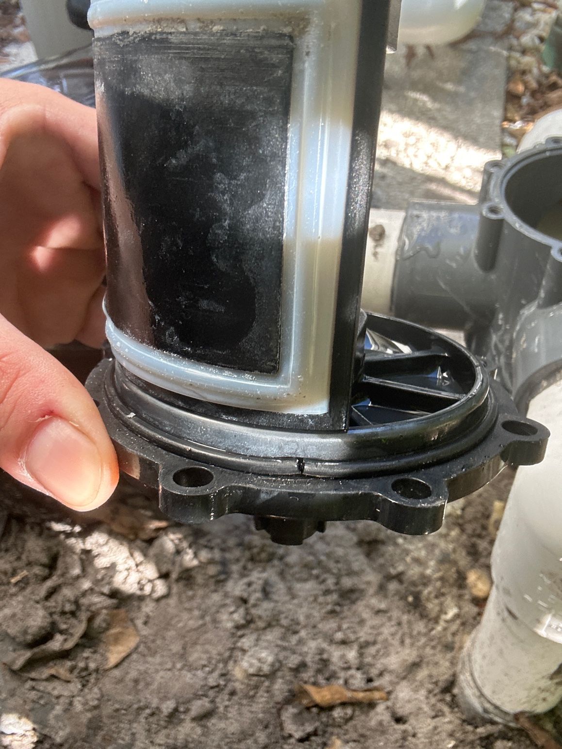 A hand holds a pool pump diverter valve assembly with a cracked plastic base plate.