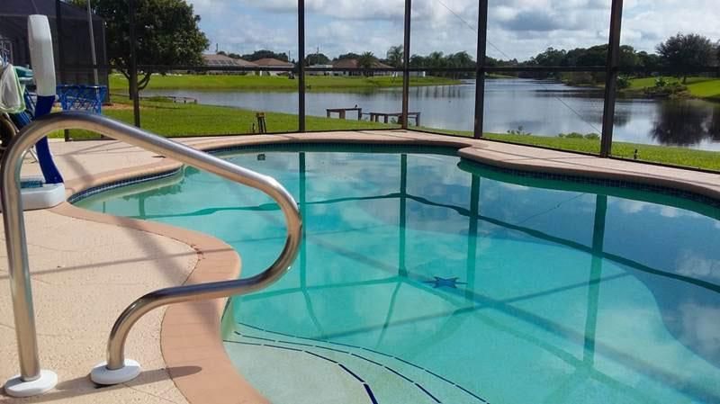 A swimming pool inside a screened enclosure, with a metal railing in the foreground and a lake visible in the background.