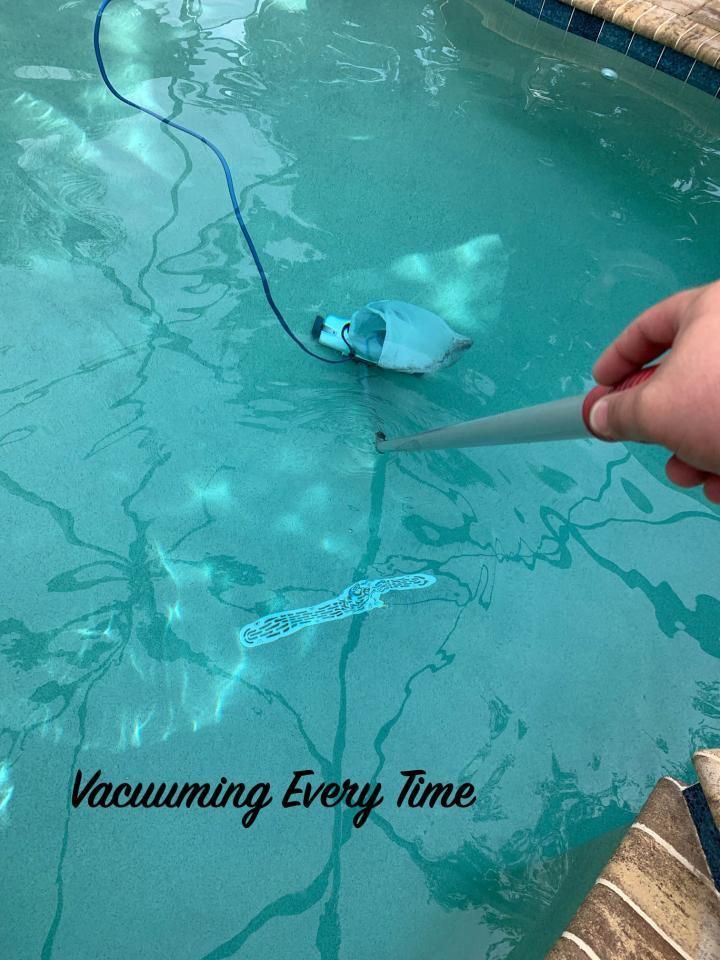 Hand vacuum skimming debris from a turquoise pool, with text “Vacuuming Every Time”