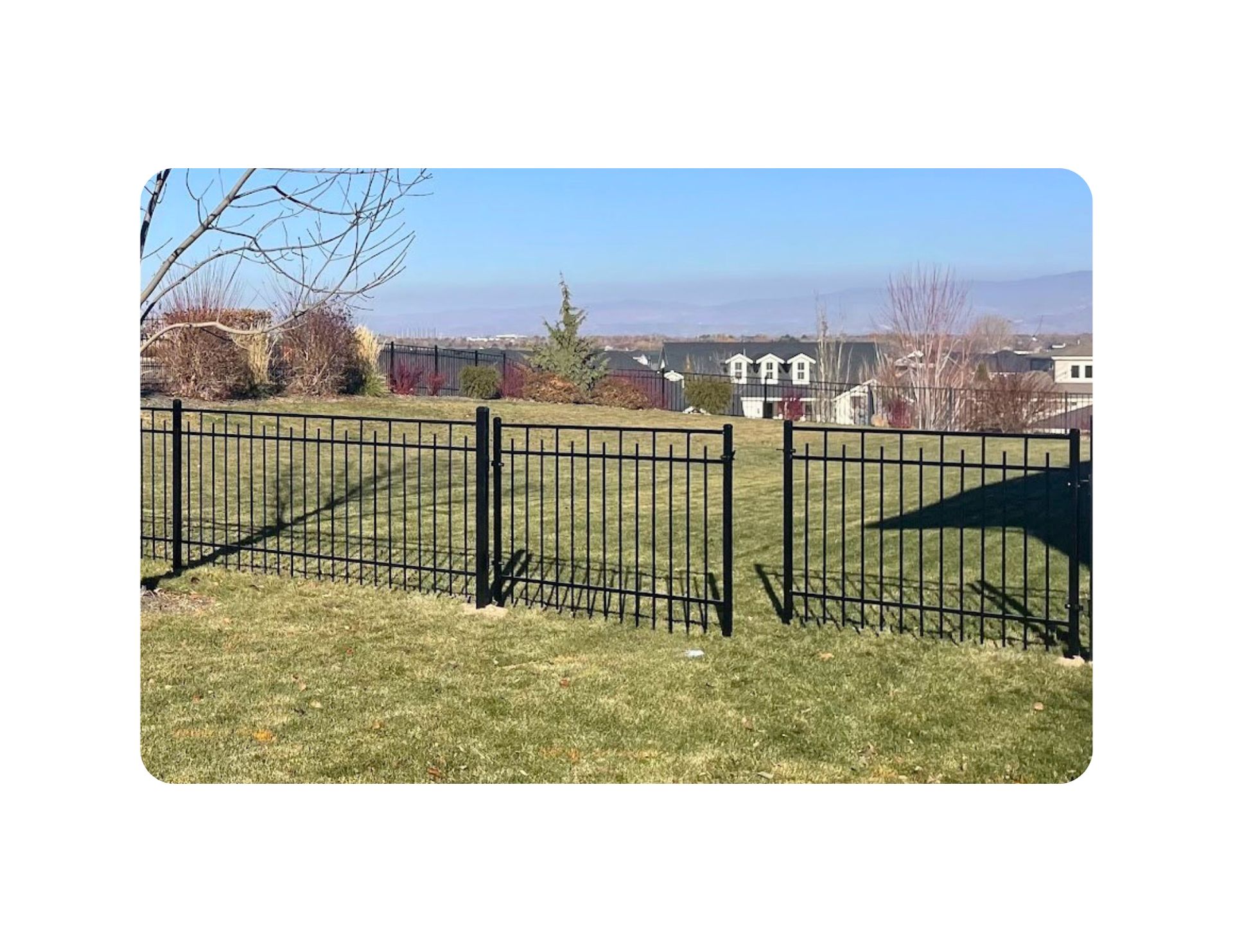 Black metal fence on a grassy lawn with a view of houses and a clear sky.