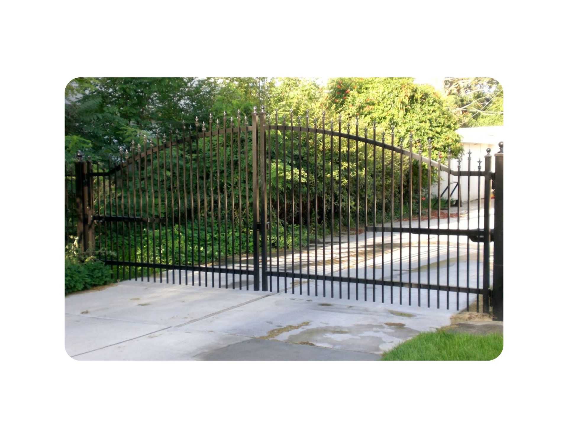 Black metal gate across a concrete driveway, leading to greenery.