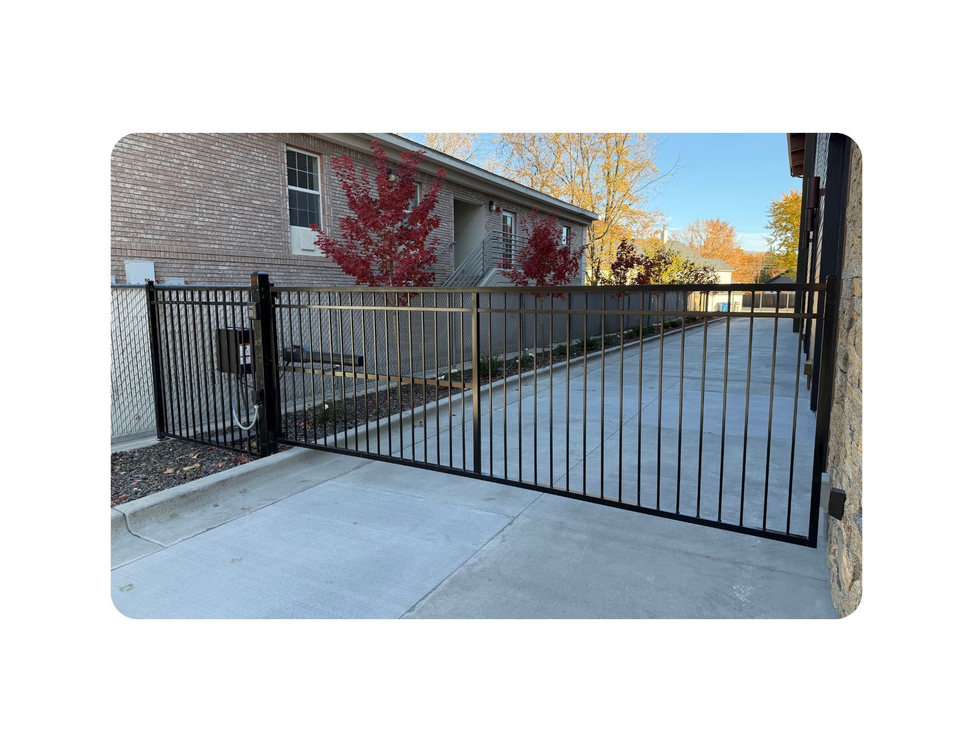 Black metal fence and gate protecting a concrete driveway next to a brick building.
