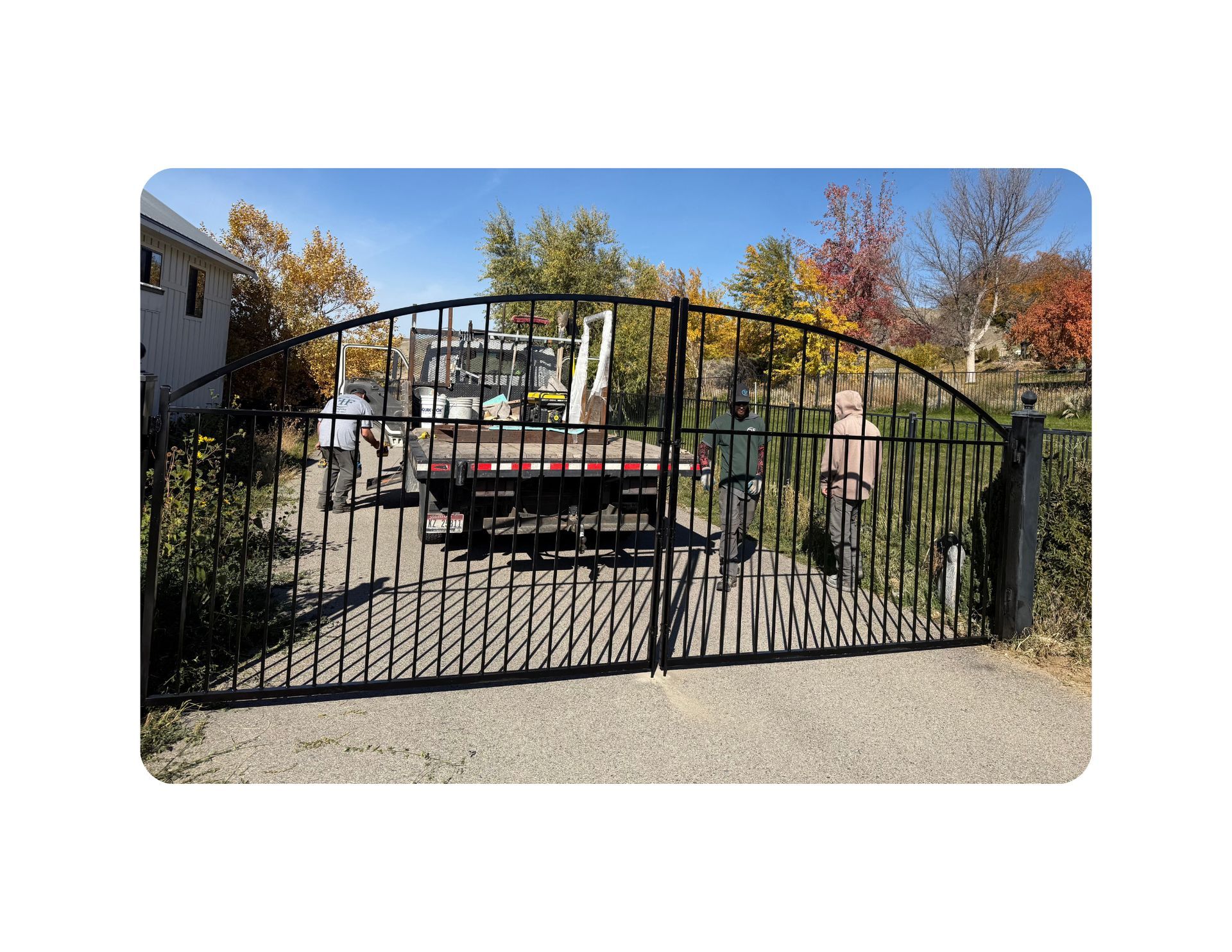 Black wrought iron gate, arched top, set in concrete, leading to a backyard.