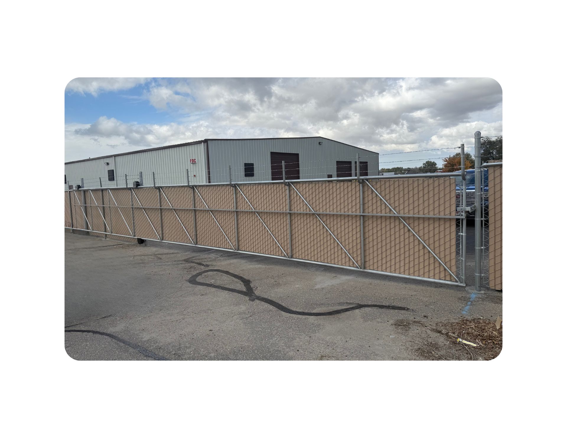 Chain-link fence with tan privacy slats in front of a gray building under a cloudy sky.