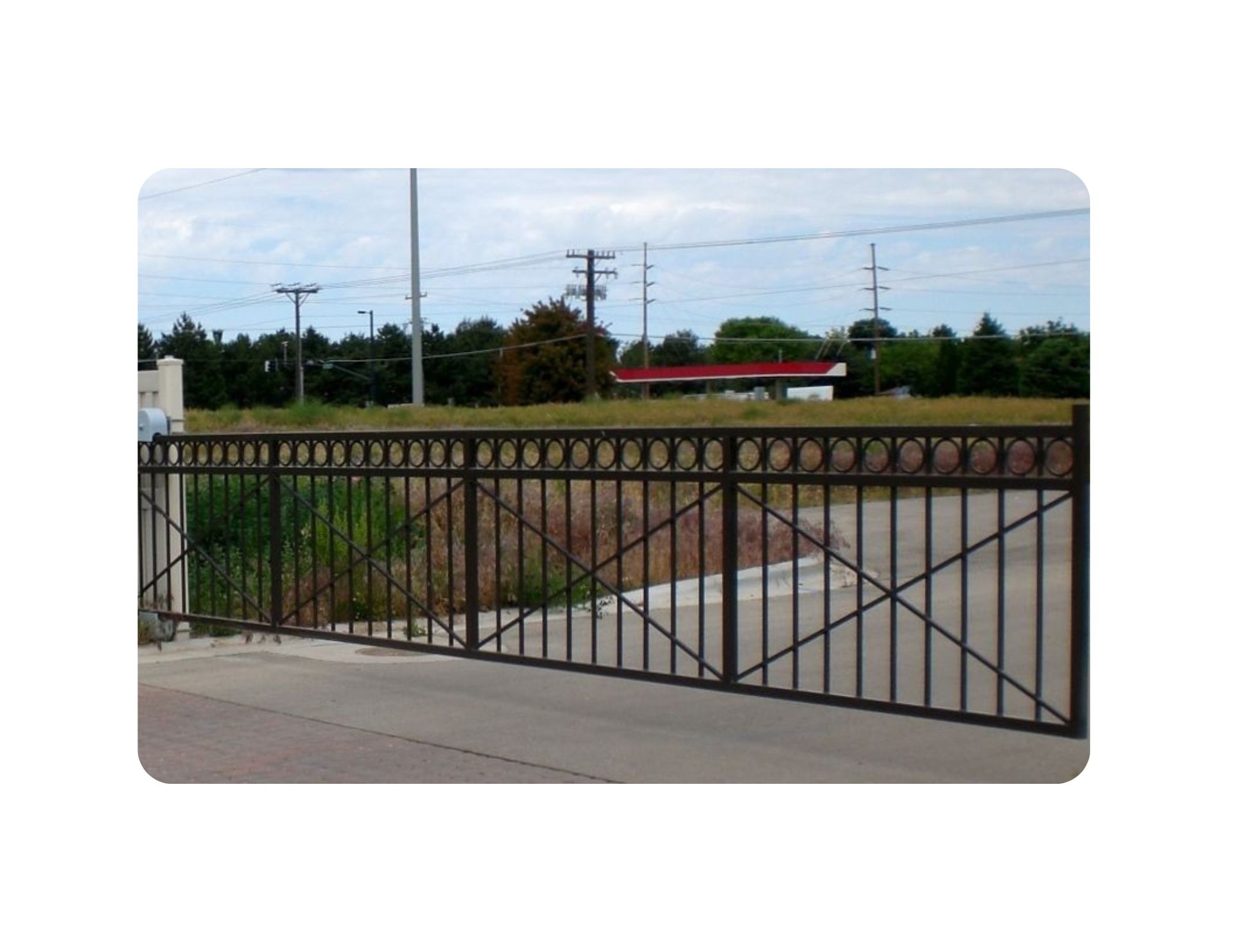 Black wrought iron gate in front of a vacant lot, with power lines and a building in the background.