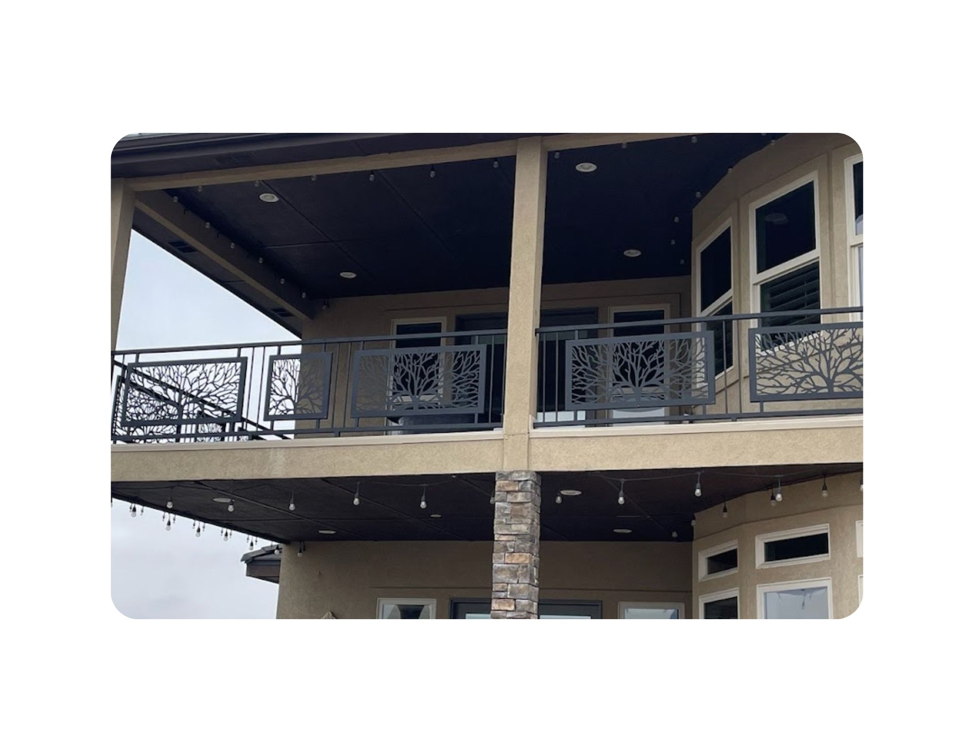 A two-story house with ornate black metal railings on a balcony. String lights are strung under the balcony.