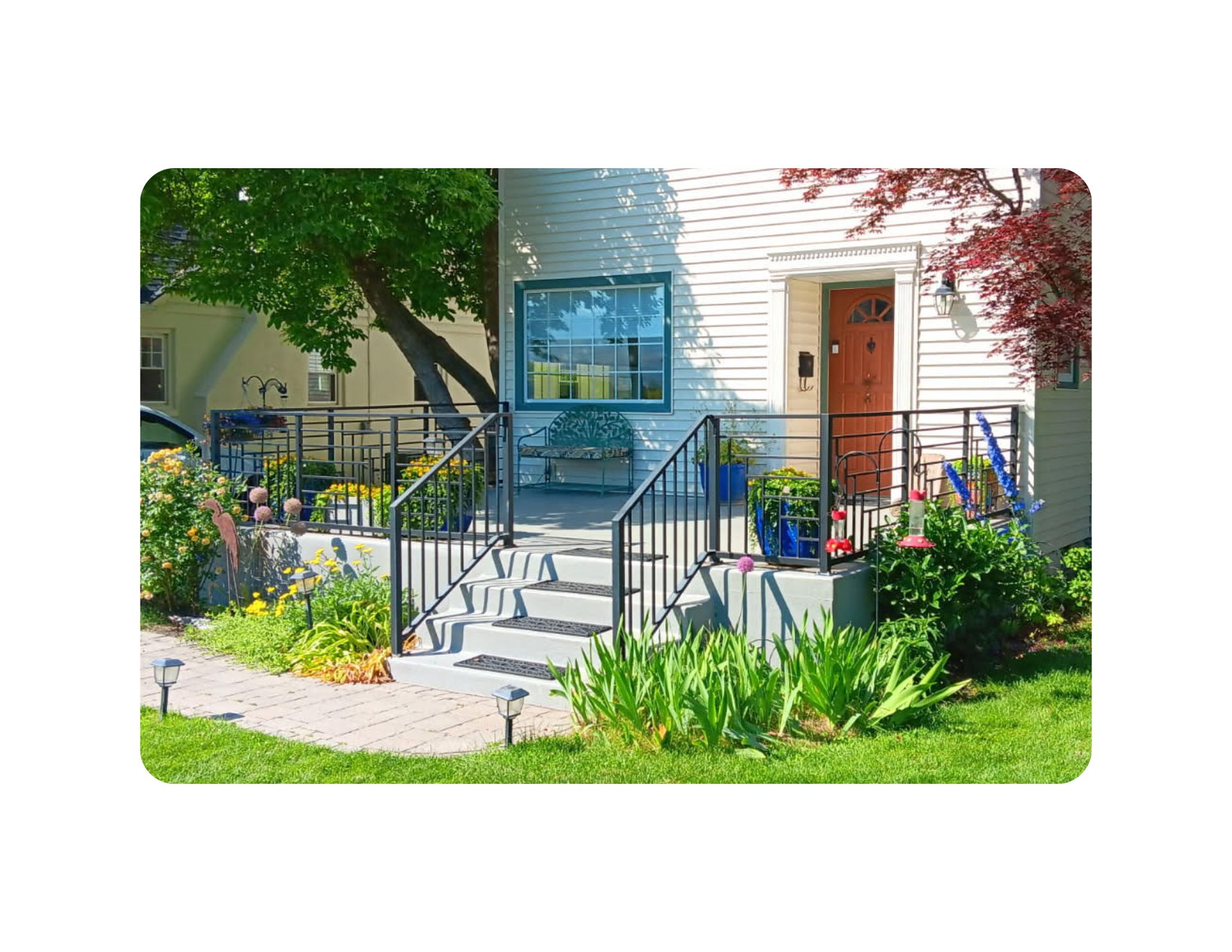 Exterior view of a house with steps and a ramp leading to the front door, with garden and bushes in front.