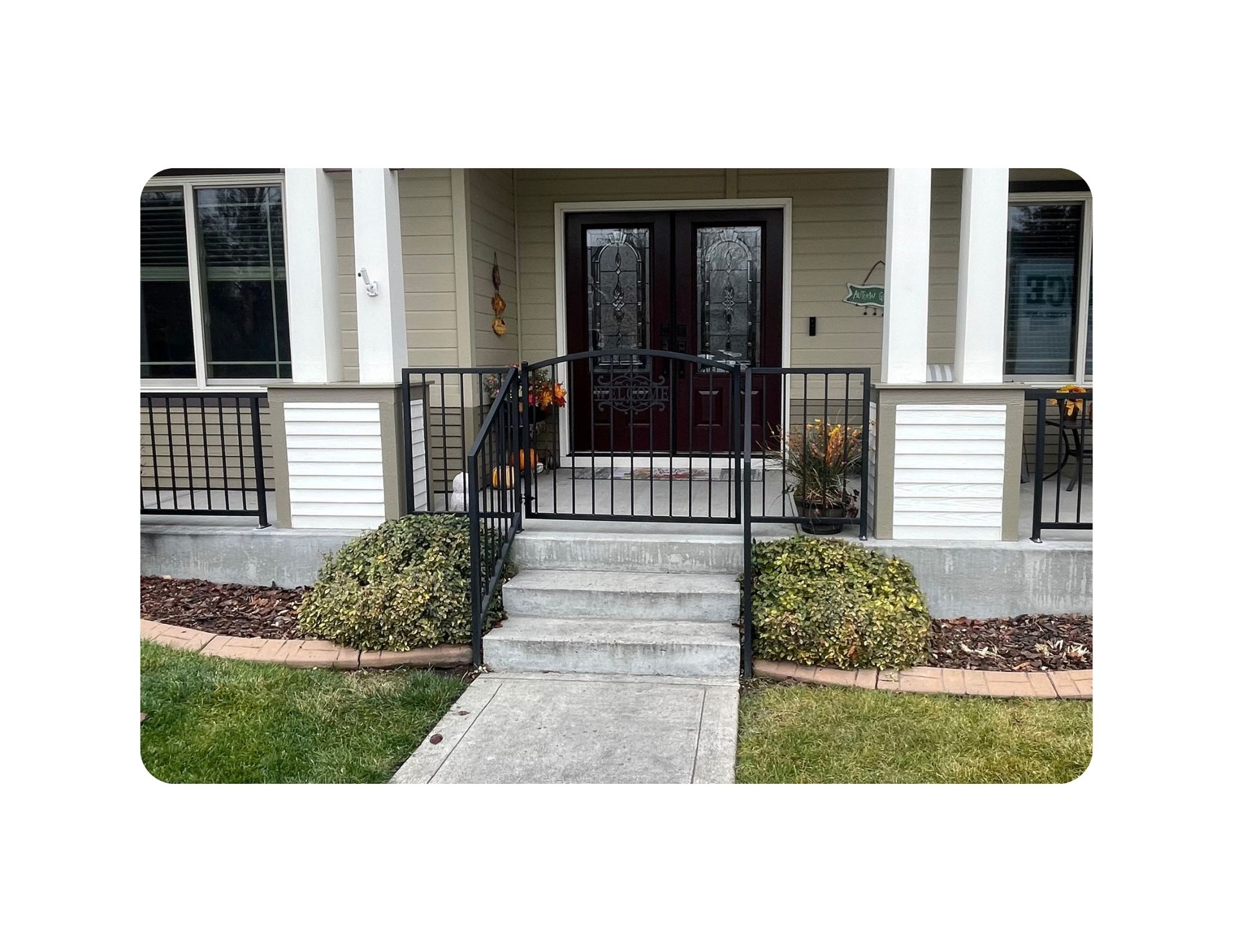 Front porch of a house with a concrete walkway and stairs, black railing, and double doors.