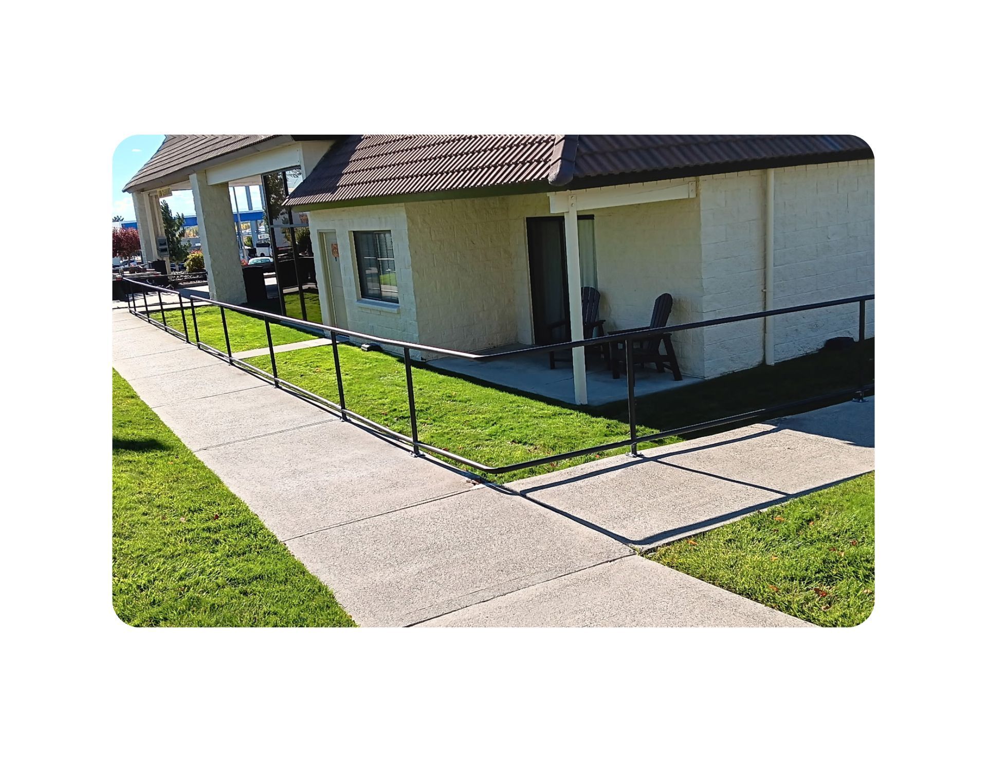 Exterior view of a building with a black railing, sidewalk, and green lawn.