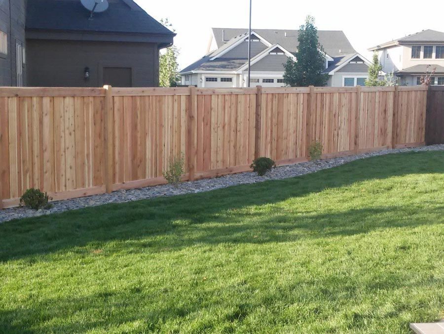 A wooden fence surrounds a lush green lawn in a backyard.