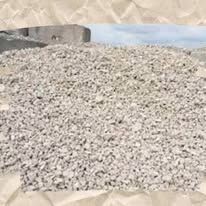 Pile of light gray gravel in front of a concrete structure and a hazy blue sky.