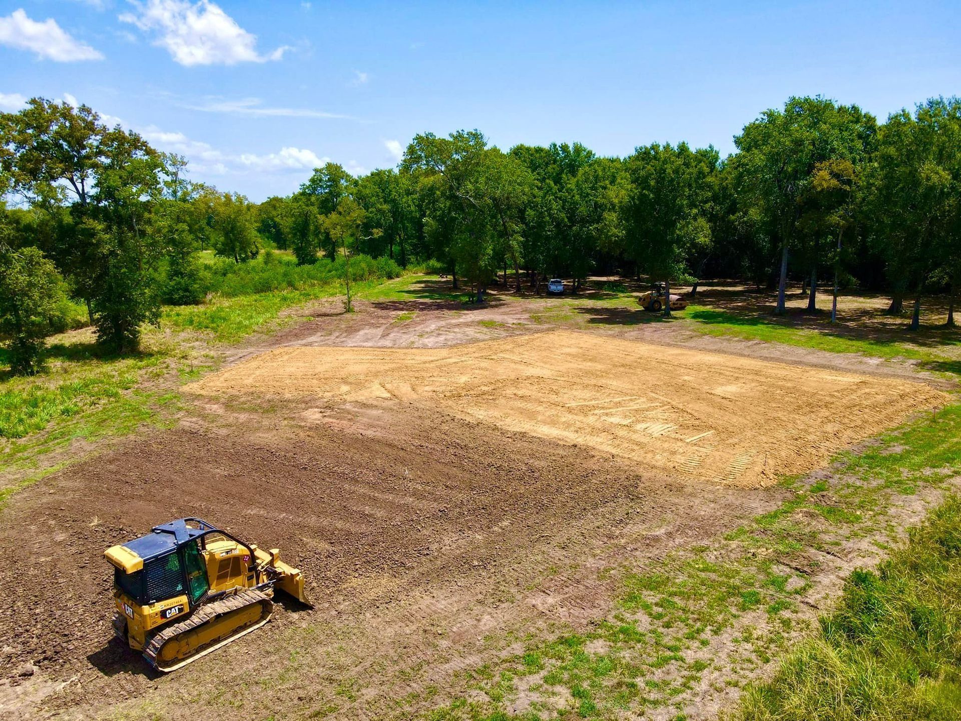 A bulldozer clearing a patch of land surrounded by trees on a sunny day.