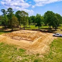 Cleared land for construction, surrounded by trees under a partly cloudy sky.