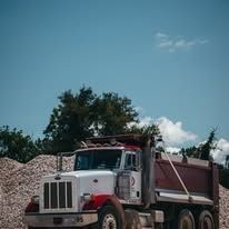 Red and white dump truck parked on gravel under a blue sky.