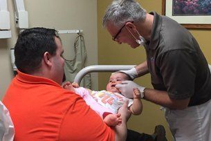 A man is holding a baby while a doctor examines it.
