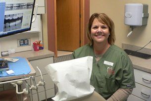 A woman is sitting in a dental chair holding a bag and smiling.