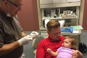 A man is holding a baby while sitting in a dental chair.