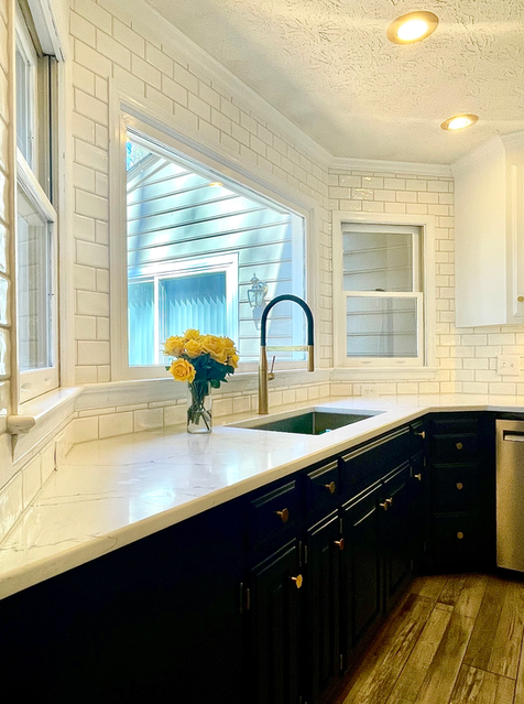 Bright white kitchen with black cabinets, large window, sink, and yellow flowers on the counter