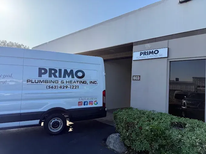 A white Primo Plumbing & Heating van parked in front of a building with a matching company sign and address number 913.