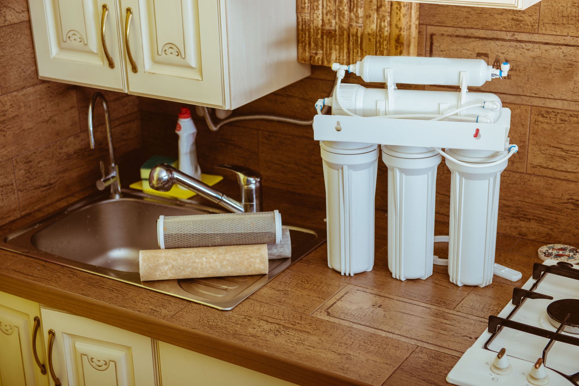 A water filtration system sits on a kitchen counter next to a sink with two used, discolored filter cartridges.