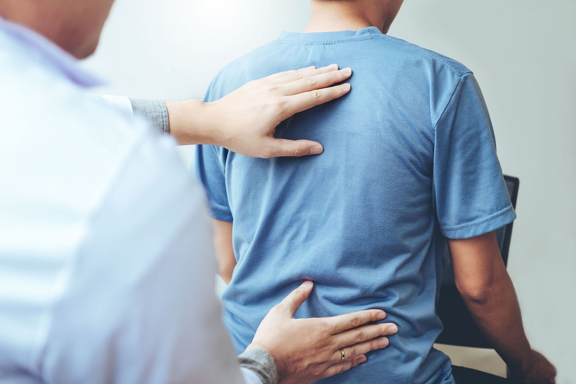 A man in a blue shirt is getting his back examined by a doctor.