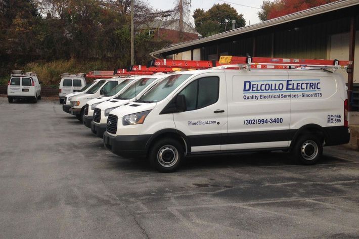 A row of delcollo electric vans parked in a parking lot