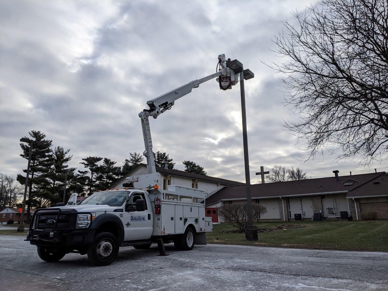 A white truck with a crane attached to it is working on a street light.