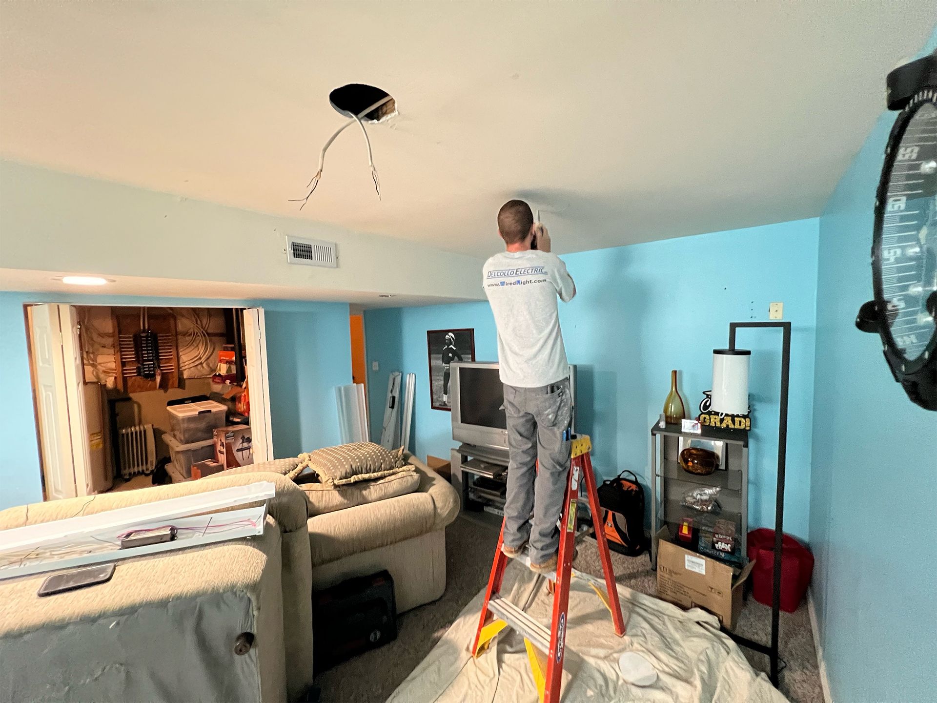A man is standing on a ladder in a living room.
