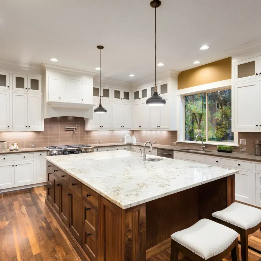 A kitchen with white cabinets and a large island with marble counter tops.
