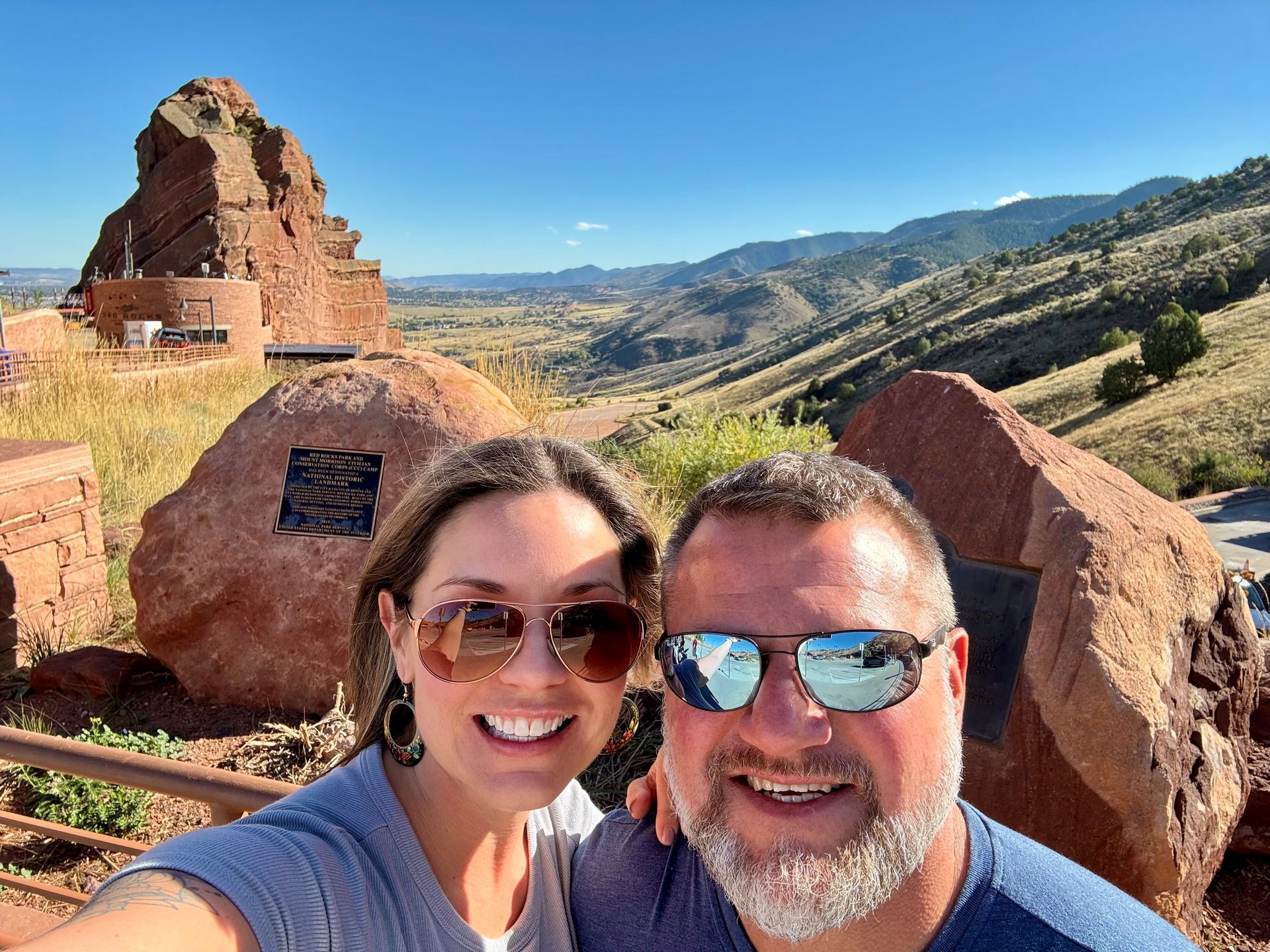 Couple taking a selfie with Red Rocks Amphitheatre and mountain vista in background.