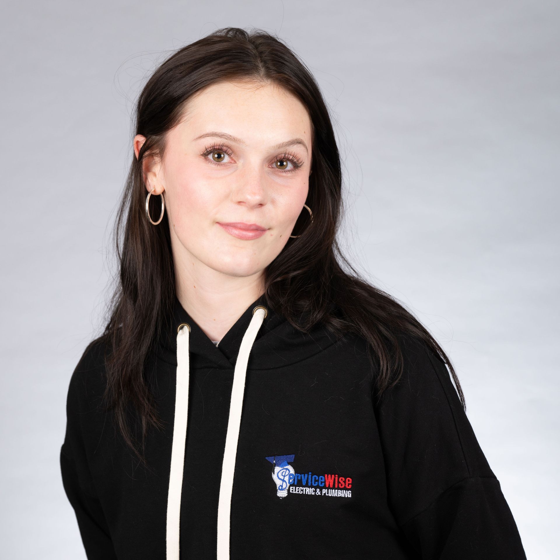 Woman with dark hair, wearing a black hoodie with a logo, smiles against a gray background.