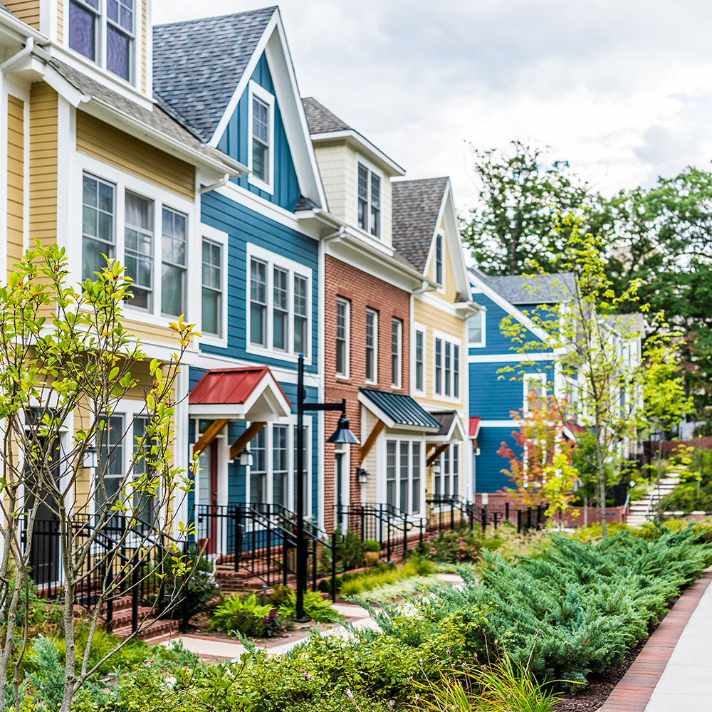 Row of colorful townhouses with landscaped front yards and a sidewalk.