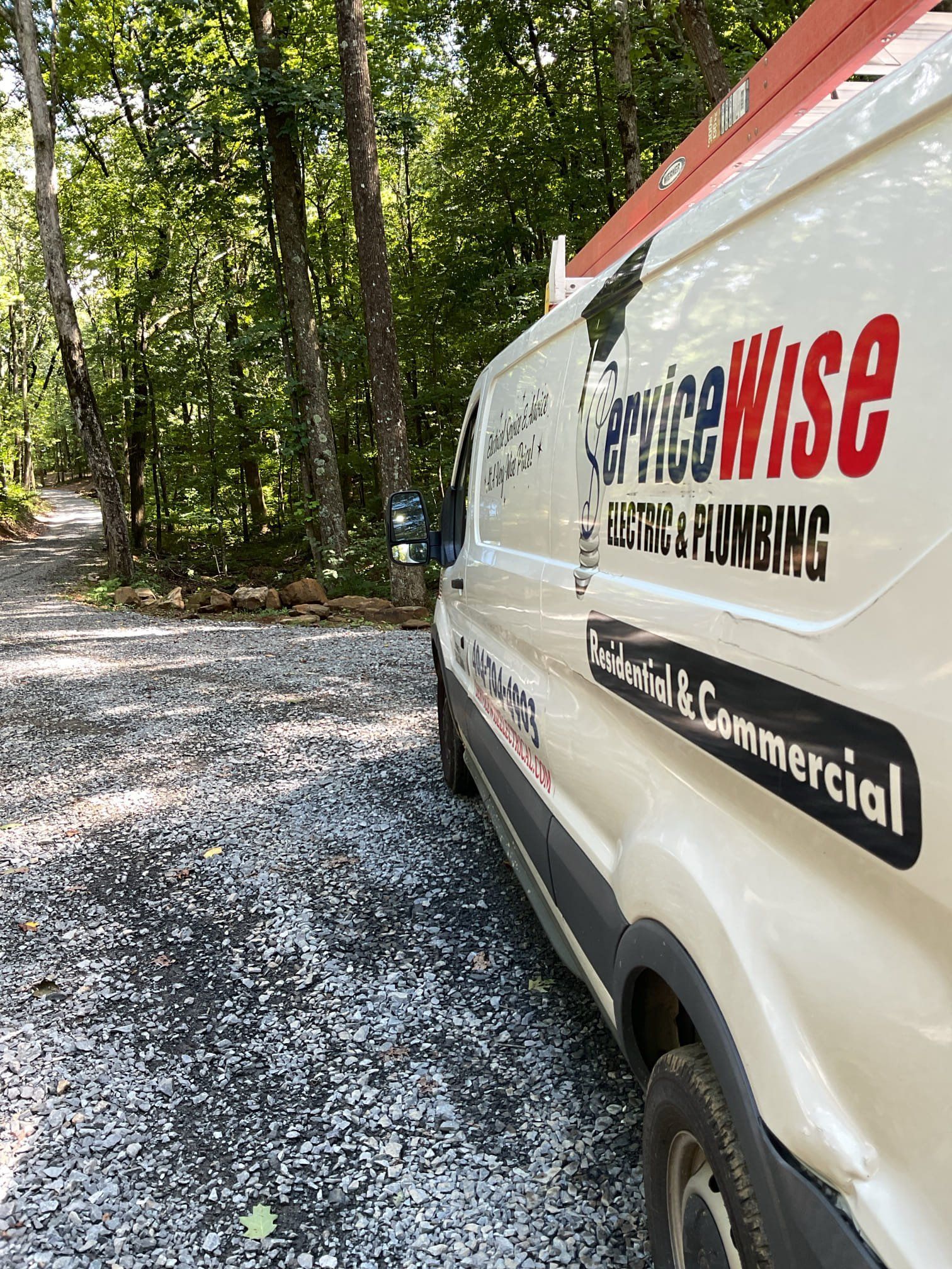 White ServiceWise van parked on a gravel road in a wooded area. Red and black logo on the side.