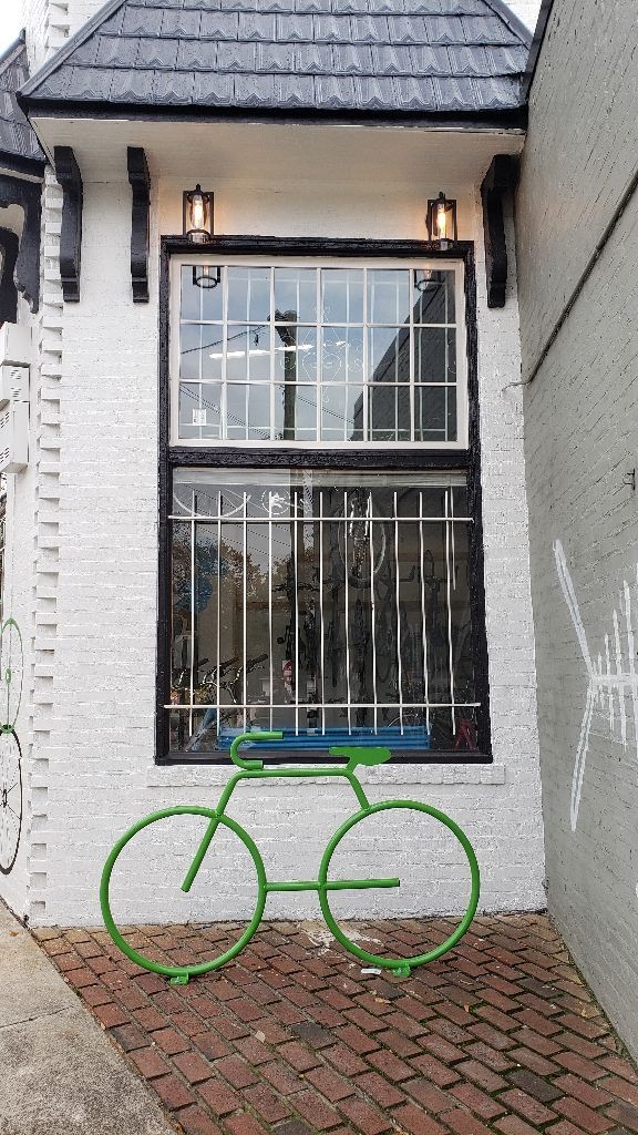 Green bicycle sculpture outside a white brick building with a large window.